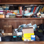 Armoire très encombrée avec de divers objets : plateaux, albums photos, vieux téléphones, souvenirs, cadeaux, etc.