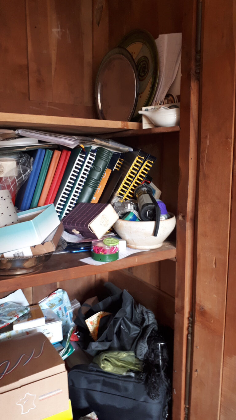 Armoire très encombrée avec de divers objets : plateaux, albums photos, vieux téléphones, souvenirs, cadeaux, etc.