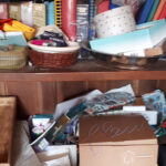 Armoire très encombrée avec de divers objets : plateaux, albums photos, vieux téléphones, souvenirs, cadeaux, etc.