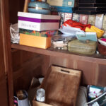 Armoire très encombrée avec de divers objets : plateaux, albums photos, vieux téléphones, souvenirs, cadeaux, etc.