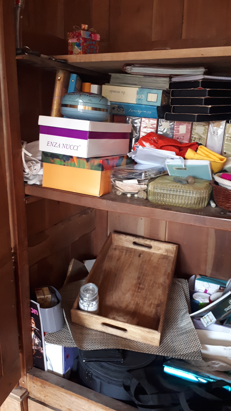 Armoire très encombrée avec de divers objets : plateaux, albums photos, vieux téléphones, souvenirs, cadeaux, etc.